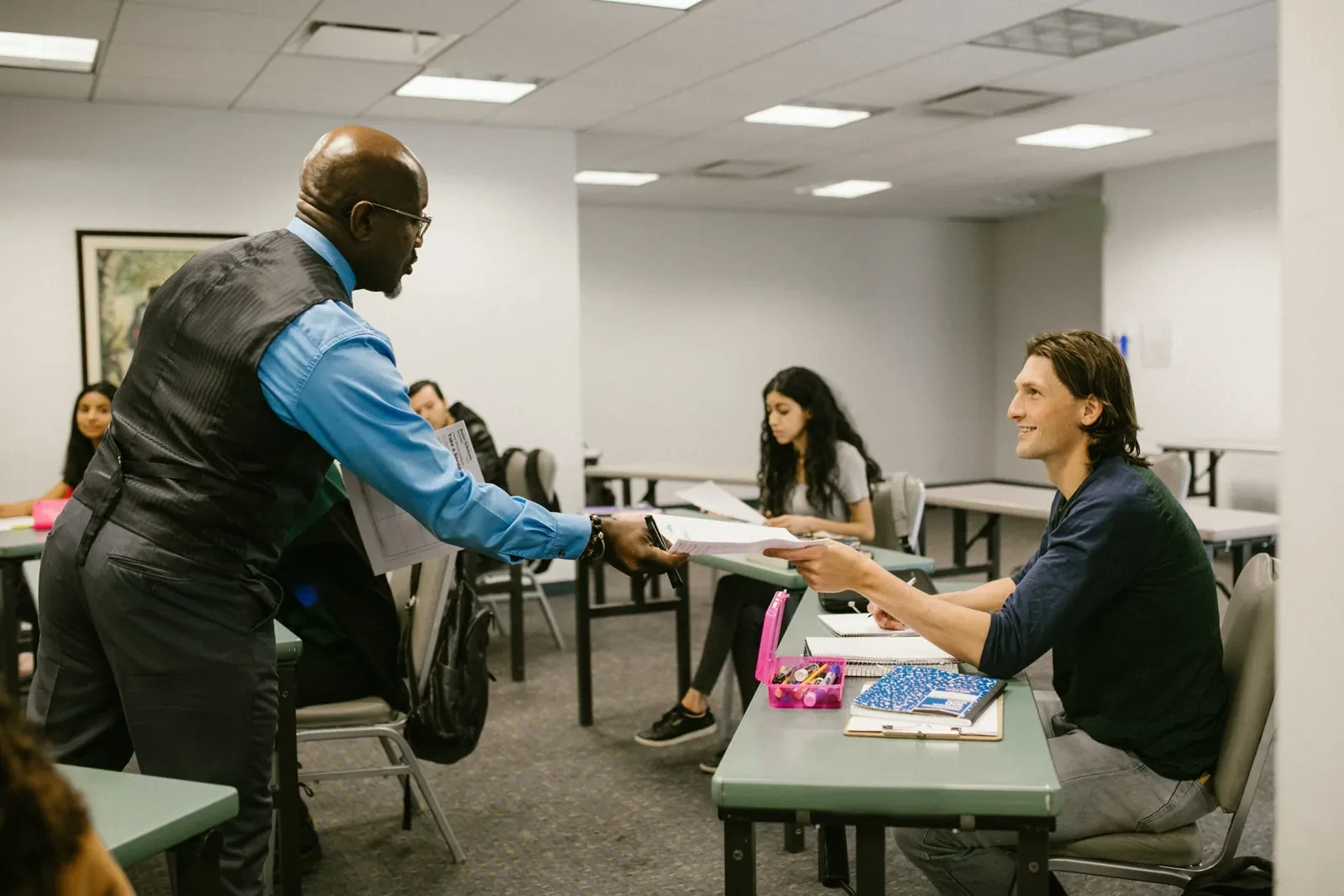 Group of adults sitting a classroom, teacher handing back paperwork for professional course