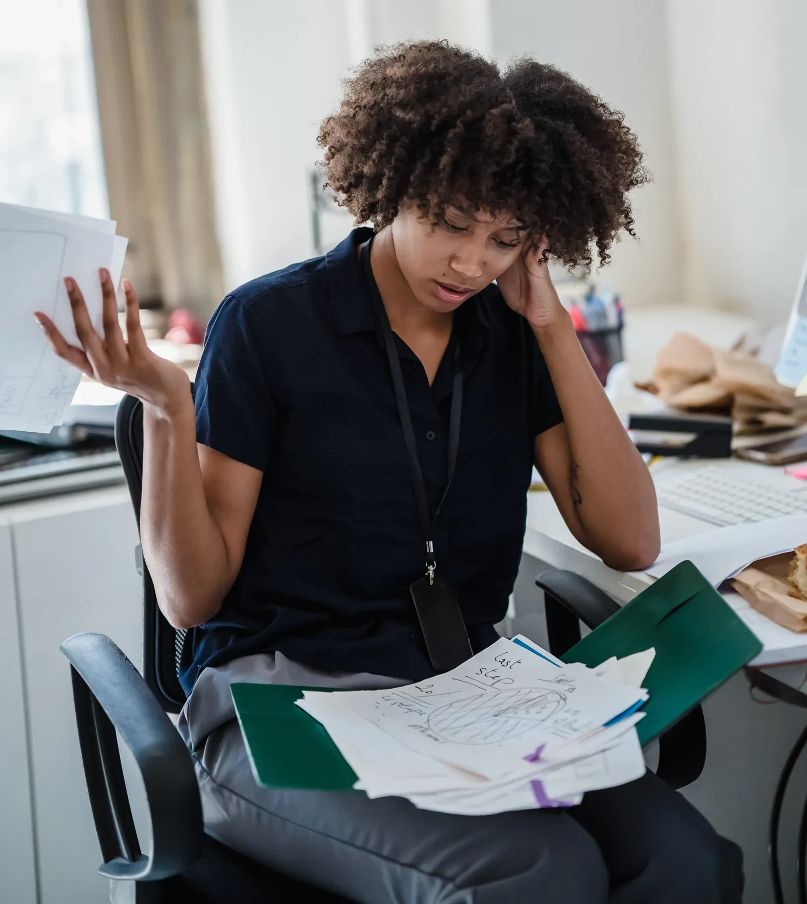 Frustrated lady sitting at her desk with a pile of paperwork on her lap