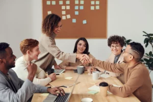Diverse coworkers talking together at table, two shaking hands
