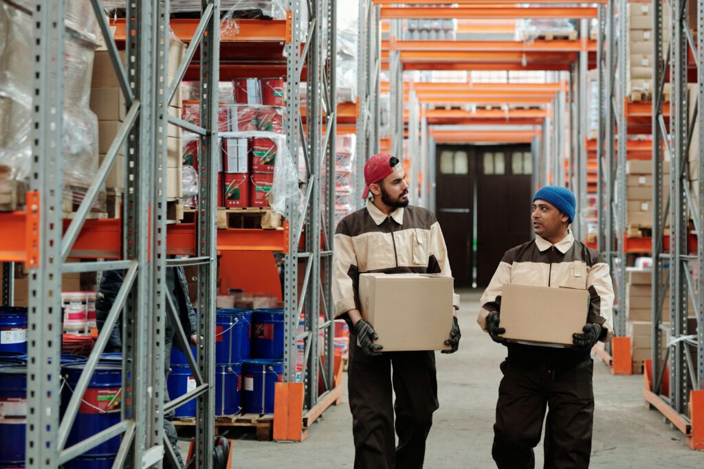 Two warehouse workers carrying boxes and talking