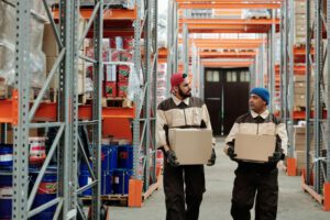 Two warehouse workers carrying boxes and talking
