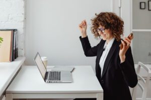 Professional woman at desk gleeful, hands up smiling at laptop